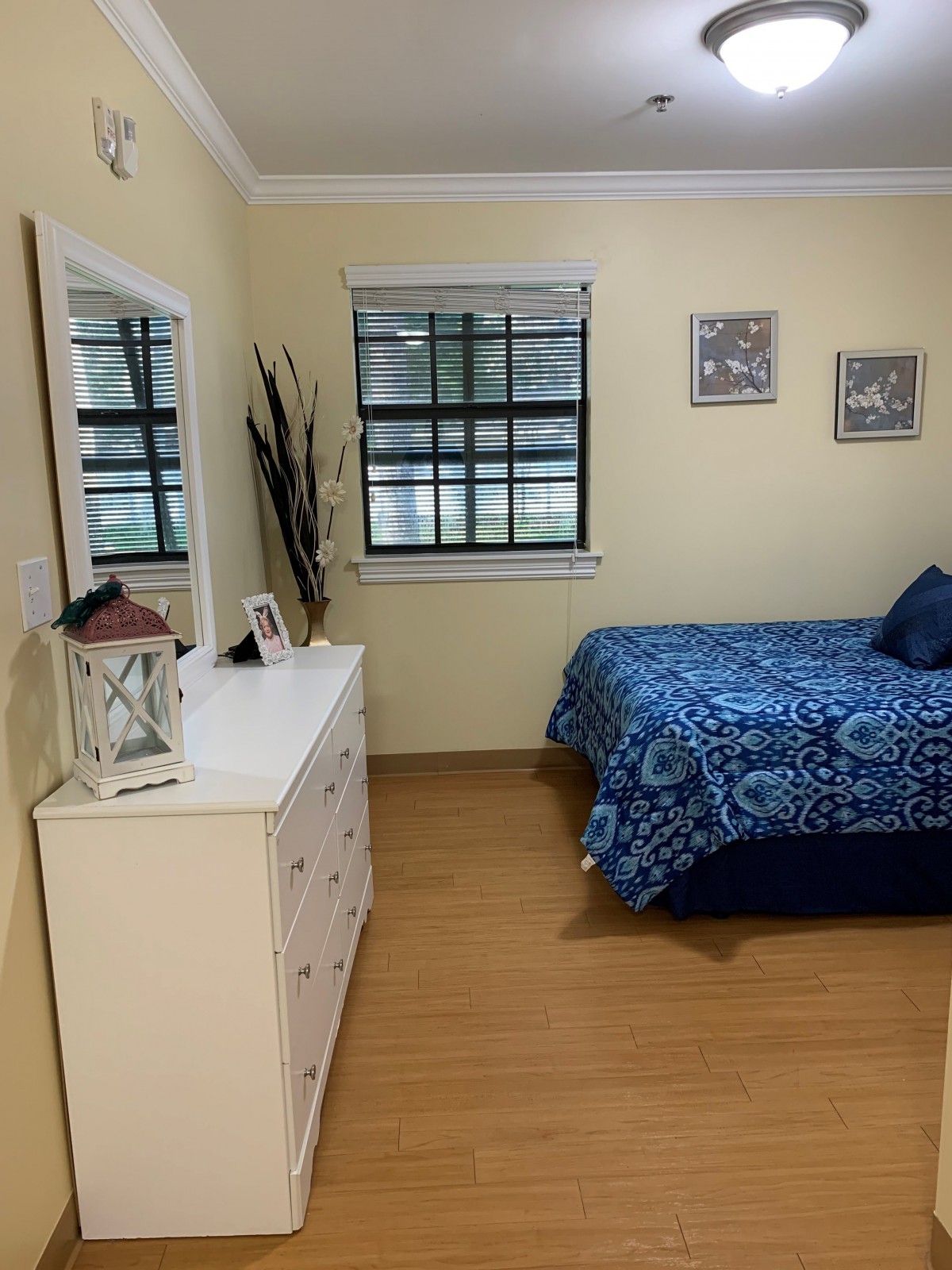 A cozy bedroom with a bed and dresser, featuring a large mirror and window.