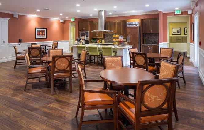A cozy dining area with wooden tables and chairs, adjacent to an open kitchen.