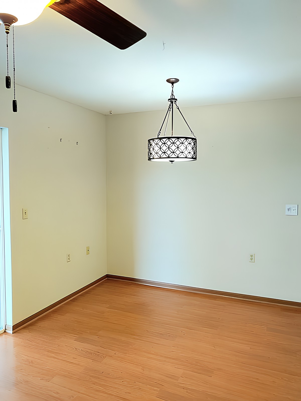 A vacant room with a wooden floor and a decorative light fixture.