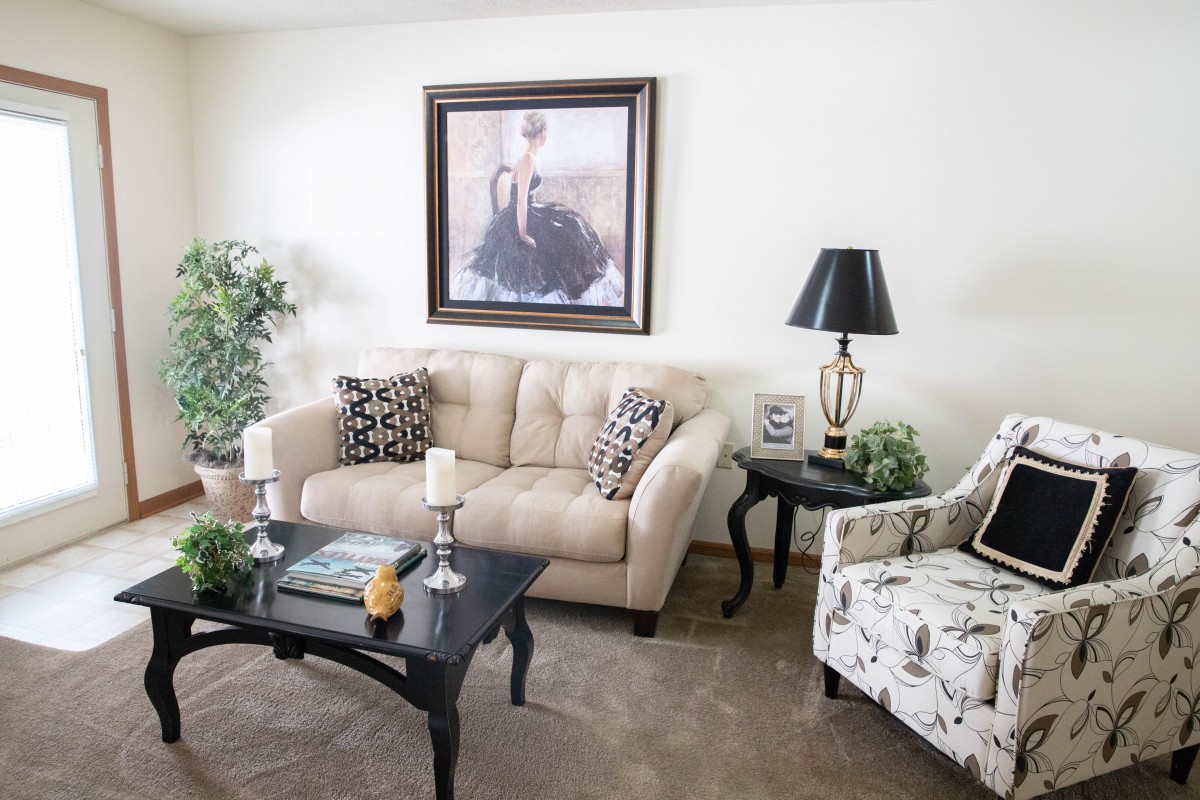 A cozy living room with a beige sofa, patterned armchair, and stylish coffee table, adorned with elegant decor and artwork.