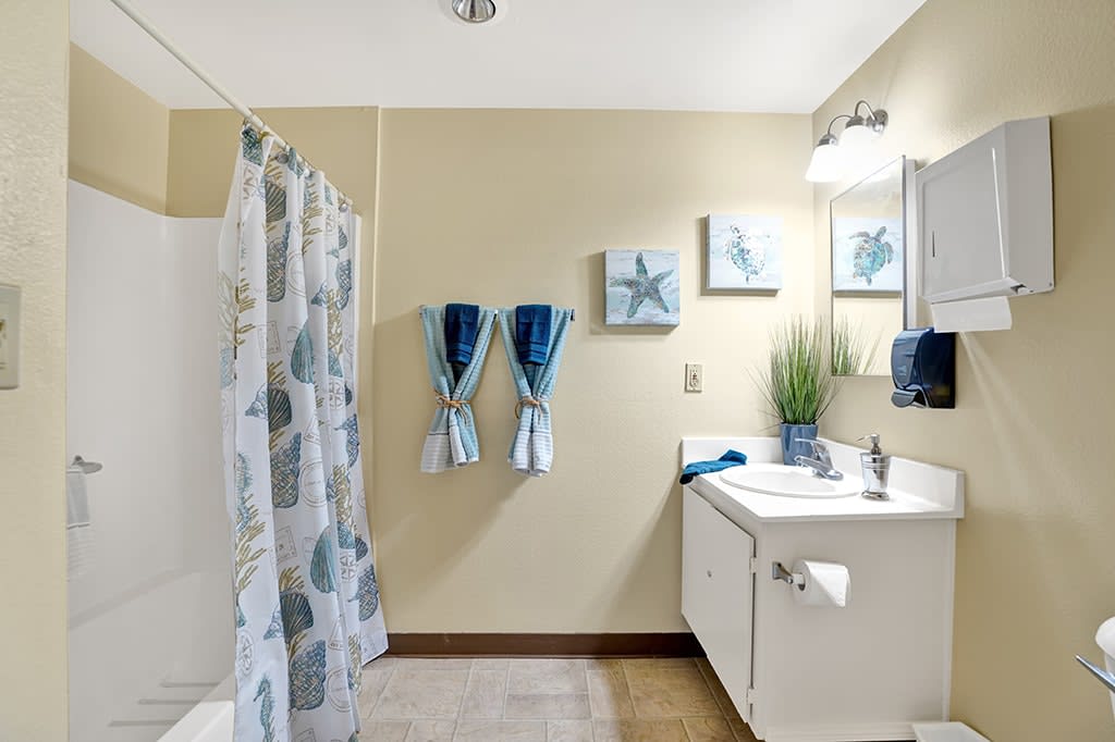 A nautical-themed bathroom featuring a shower curtain with sea patterns, starfish artwork, and neatly arranged blue towels.