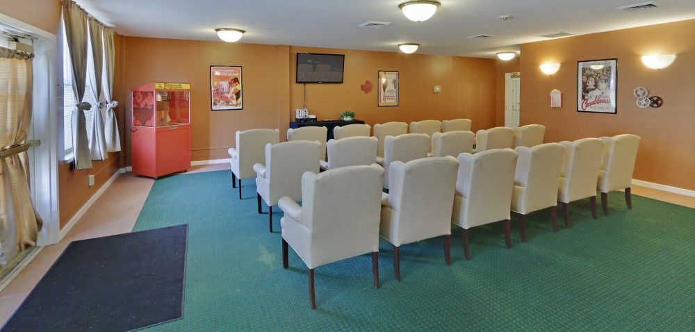 A small conference room with rows of white chairs facing a television.