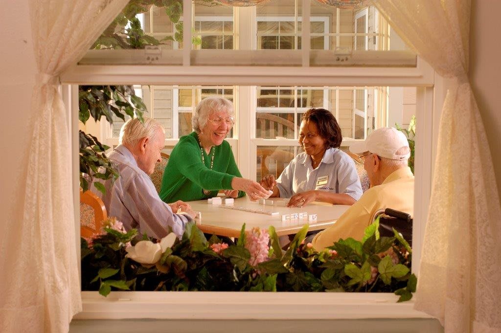 A group of elderly people enjoying a conversation around a table viewed through a window.