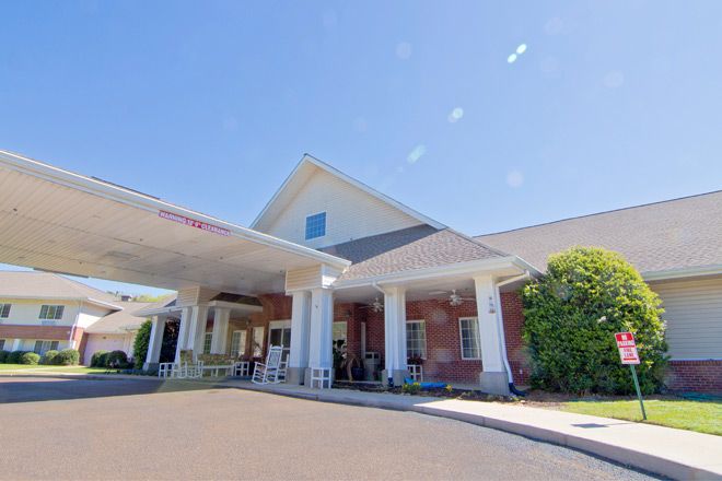 A sunny day view of a building entrance with columns and a covered driveway.