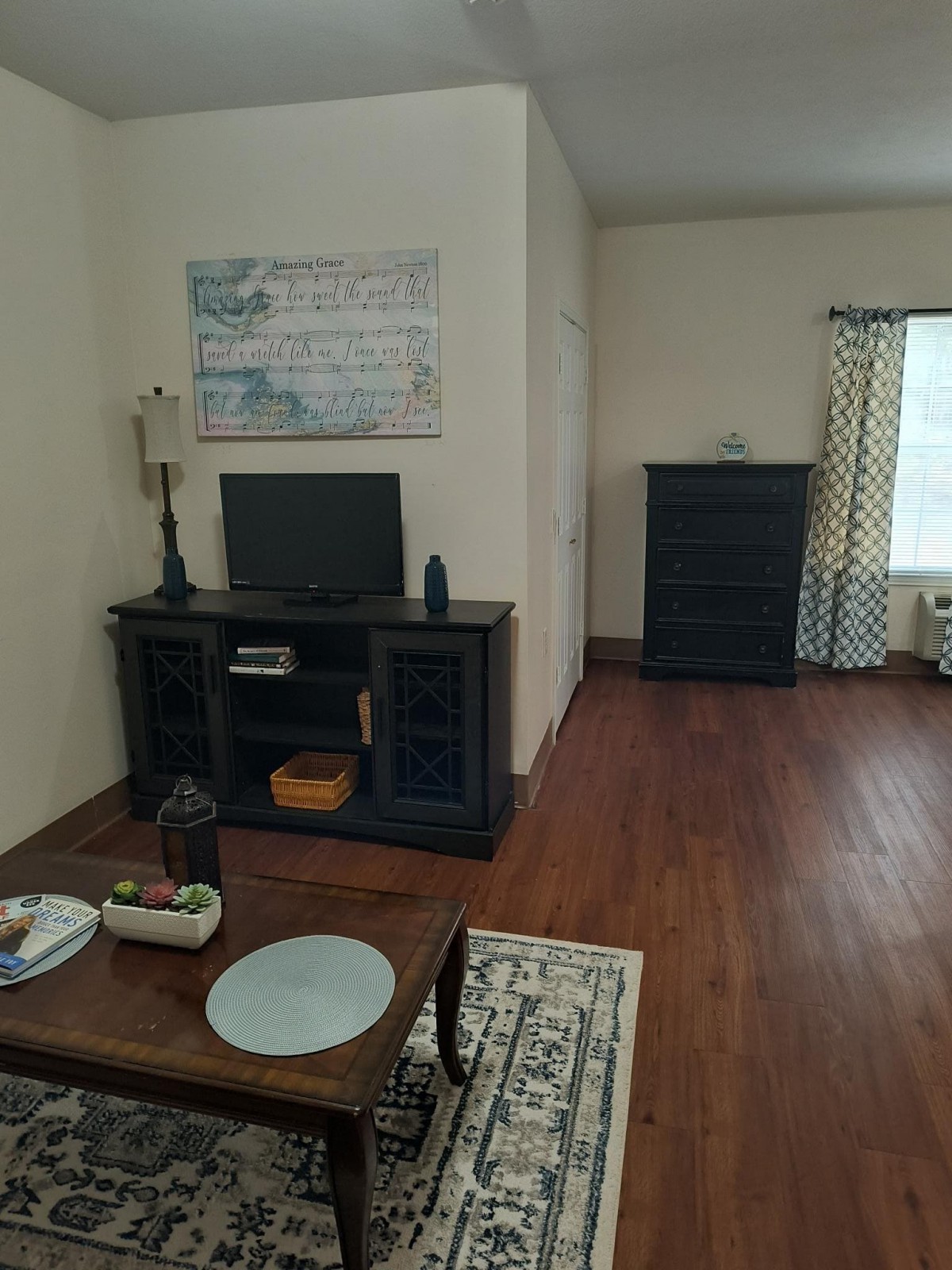 A cozy living room with a television, dark furniture, and a small dining table on a wooden floor.