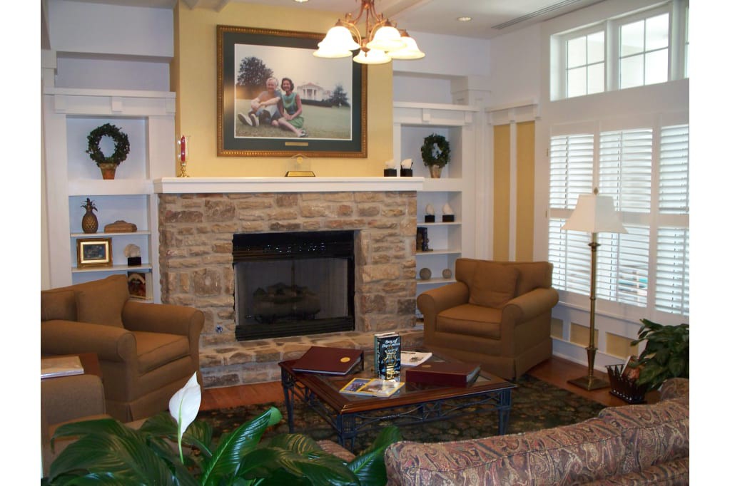 A cozy living room featuring a stone fireplace, two armchairs, and a coffee table, with a painting above the mantelpiece.