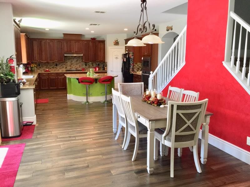 A spacious open-concept kitchen and dining area with wood flooring, featuring a bold red accent wall and elegant chandelier.