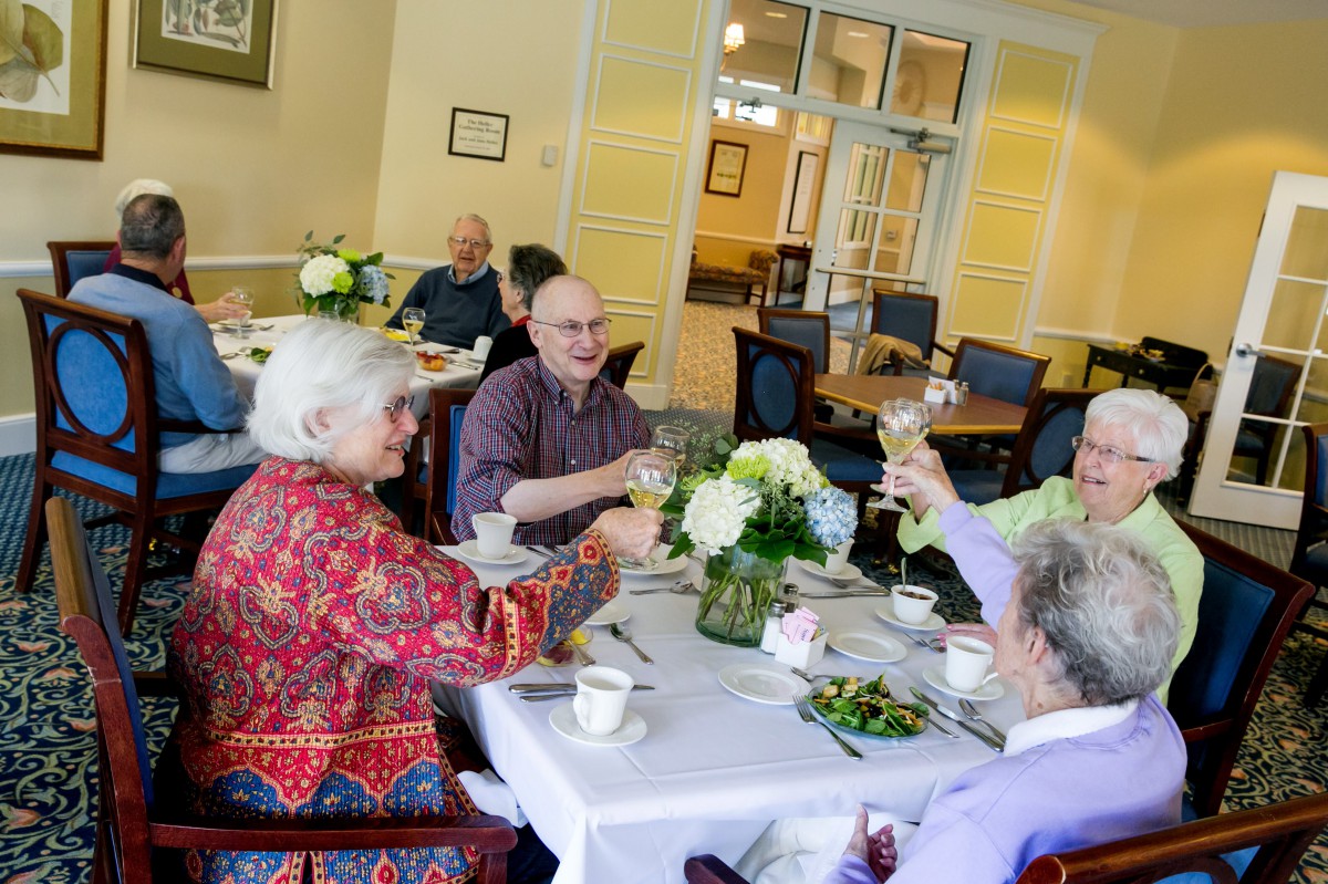 A group of seniors enjoying a meal and toasting together in a dining room.