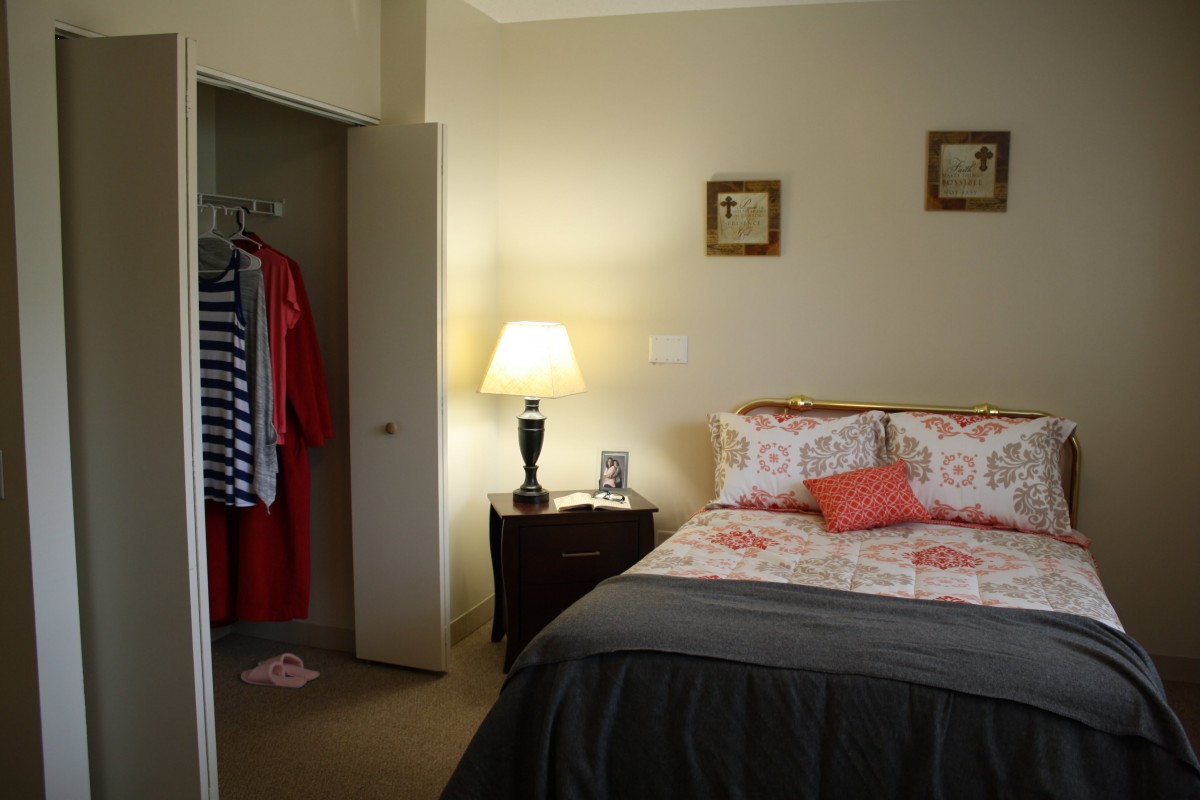 A cozy bedroom with a bed, nightstand, lamp, and open closet.
