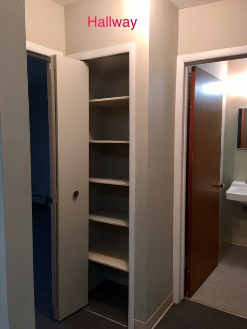 A hallway with open closet shelving and a view into a bathroom.