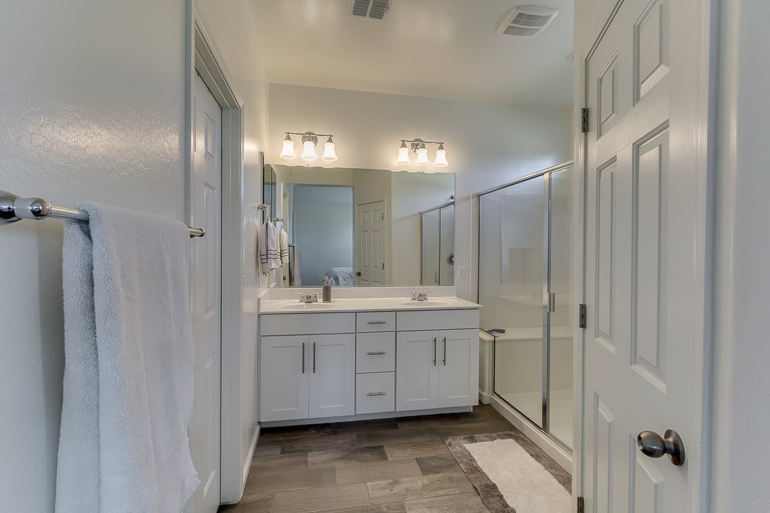 A modern bathroom with a double sink, large mirror, and a glass-enclosed shower.