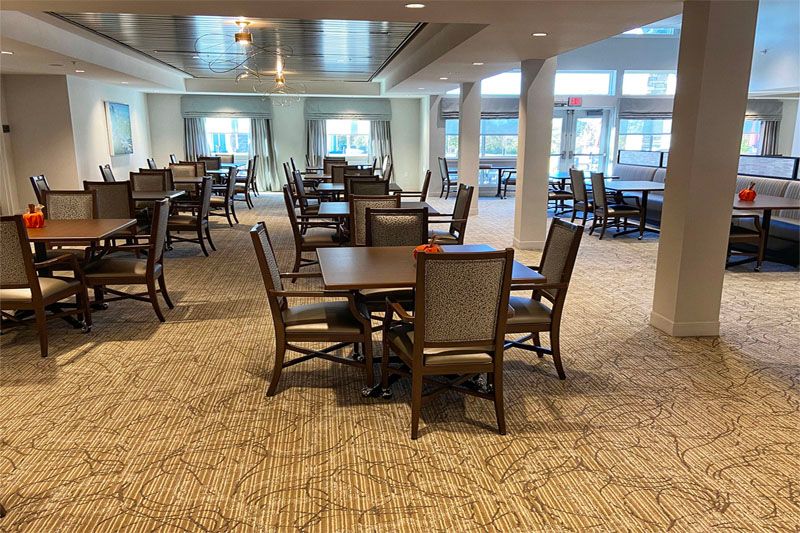 A spacious dining area featuring several tables and chairs, illuminated by natural light.