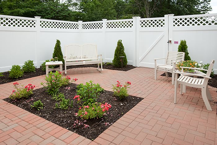 A cozy patio with white fencing, featuring benches and a small flower garden.