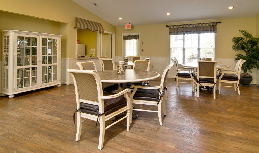 A cozy dining area with a round table and cushioned chairs, featuring large windows and wooden flooring.