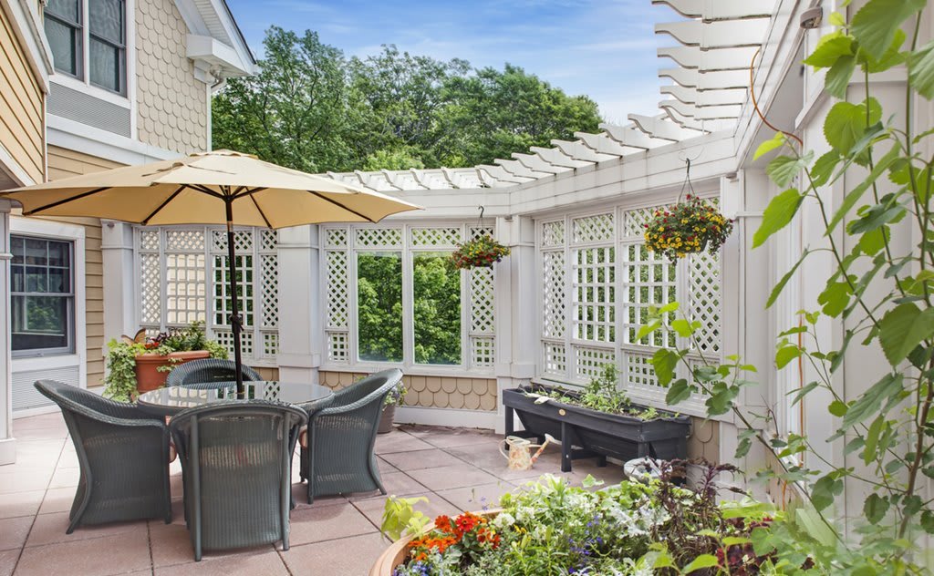 A cozy outdoor patio with a pergola, seating area, and lush greenery.