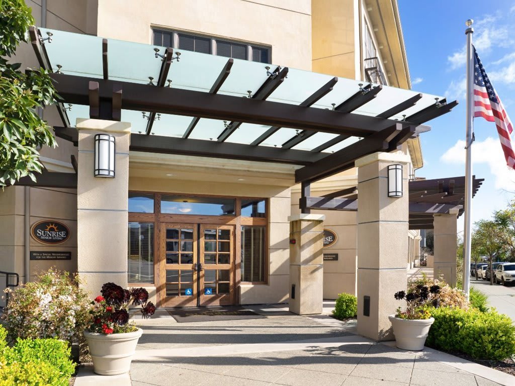 Modern building entrance with a glass canopy and landscaping.