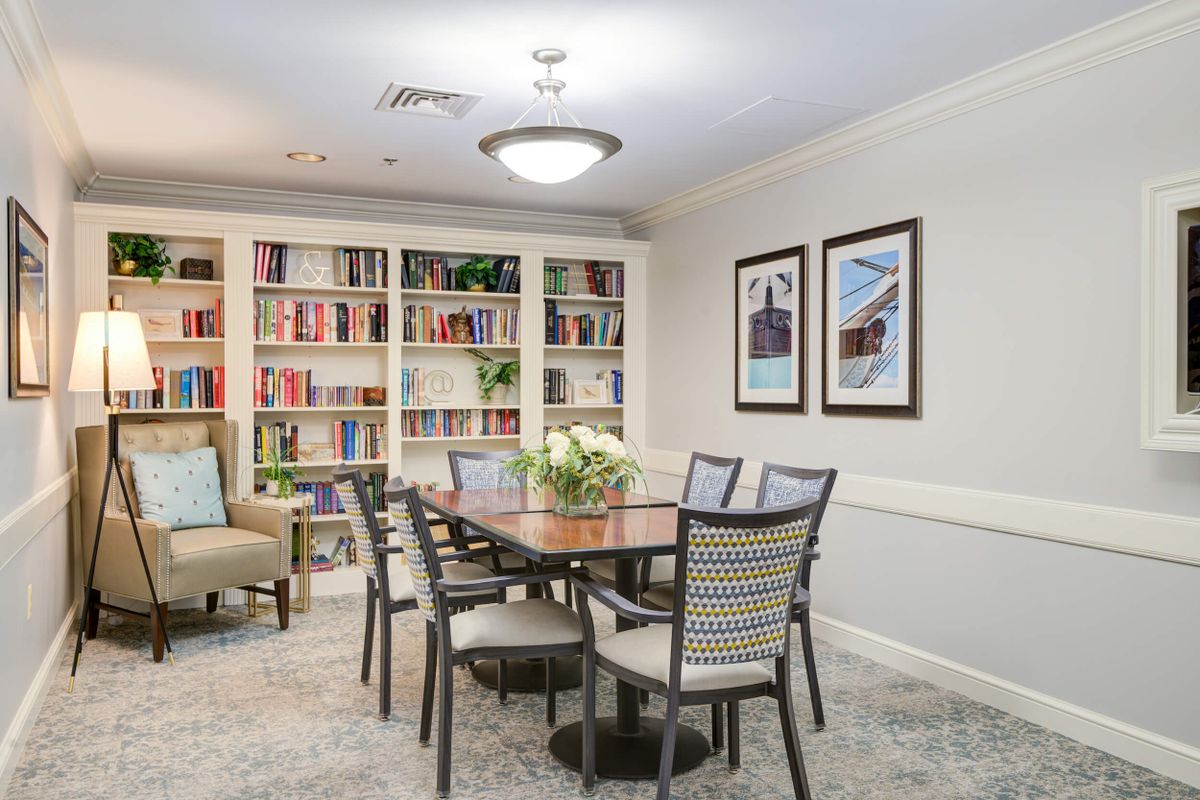 A cozy dining area with a wooden table and chairs, surrounded by bookshelves and decorated with artwork on the walls.