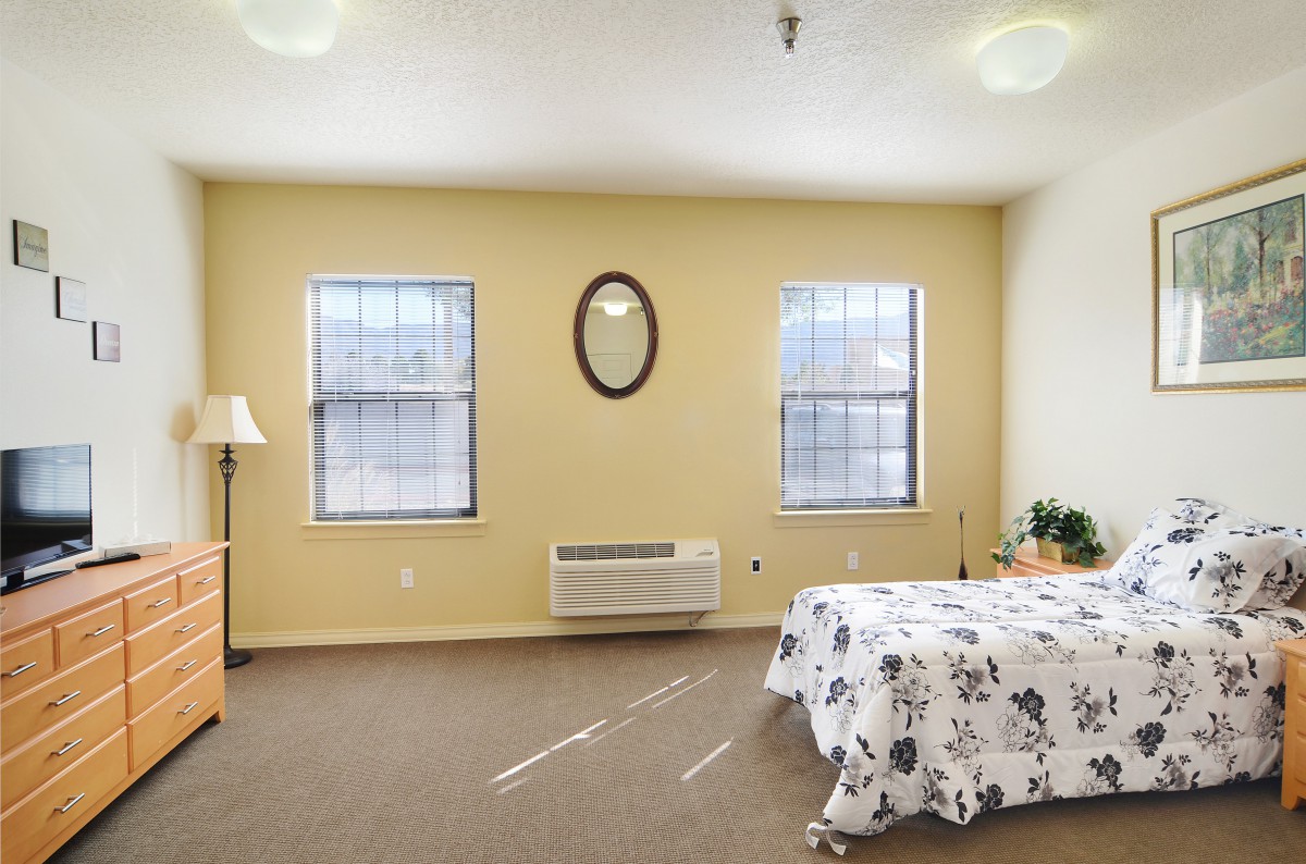 A cozy bedroom interior with a bed, two windows, and warm lighting.