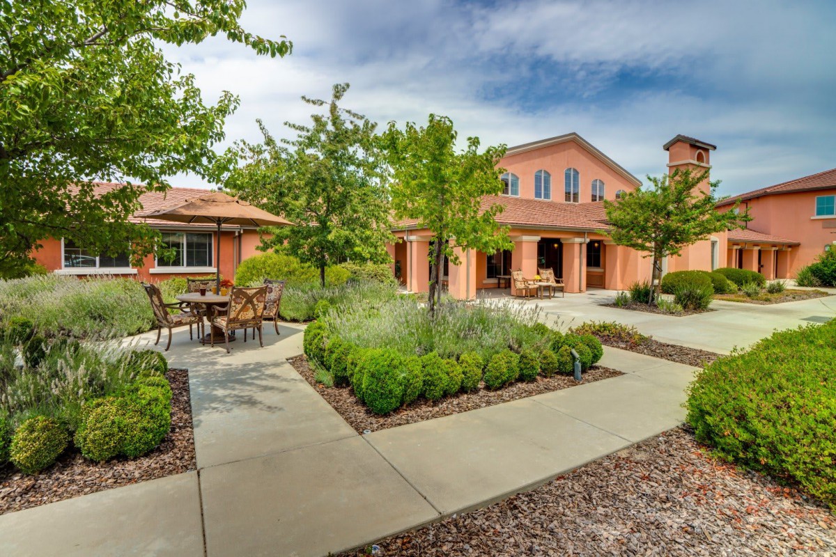 A tranquil courtyard with trees, pathways, and outdoor seating in front of a building.