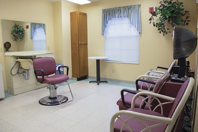 An empty hair salon with chairs and a mirror, featuring a small waiting area.