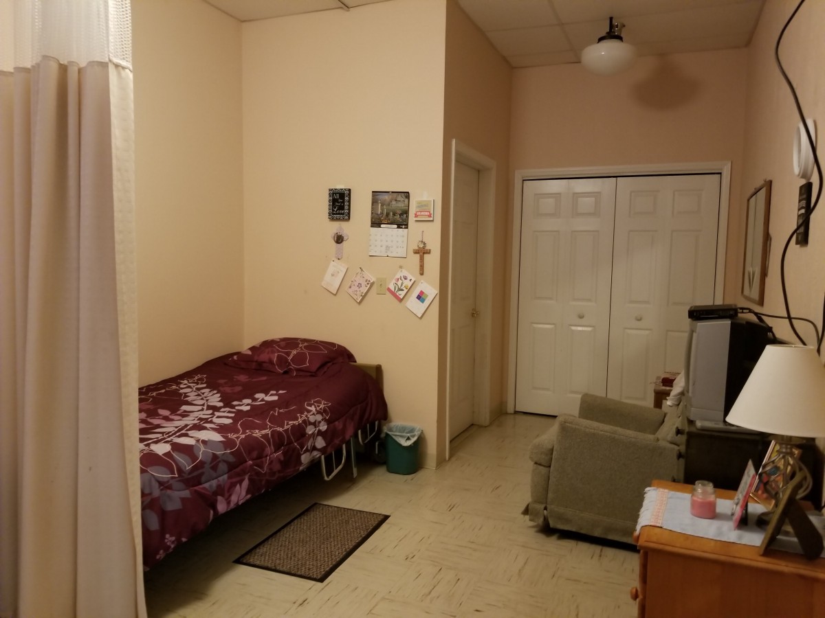 A small bedroom with a single bed, a chair, and a desk, featuring wall decorations and a closet.
