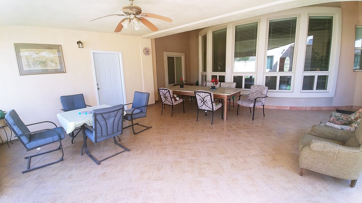 A spacious patio with multiple seating arrangements, including tables and chairs, under a ceiling fan.