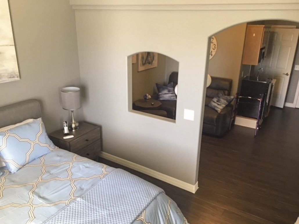 A cozy bedroom with a neatly made bed, nightstand with lamp, and decorative mirror on the wall.