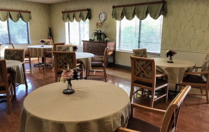 A cozy dining area with round tables, wooden chairs, and decorative curtains.