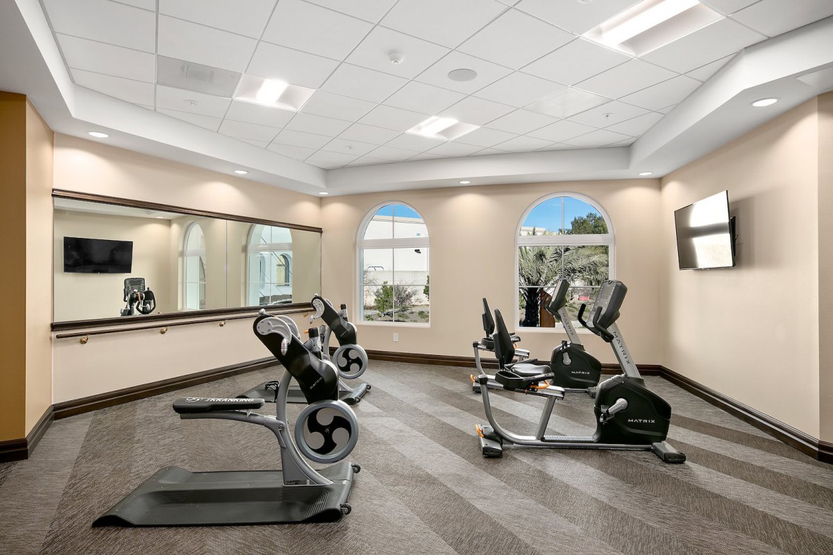 A well-lit gym featuring treadmills and exercise bikes, with large mirrors on the wall.