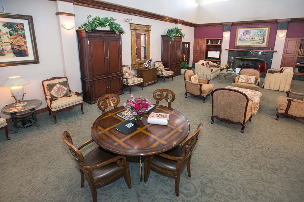 A spacious and elegantly furnished living room with a central round table, chairs, sofas, and decorative elements.