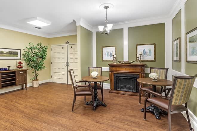 A cozy dining area with a fireplace, wooden tables and chairs, decorated with plants and artwork on the walls.