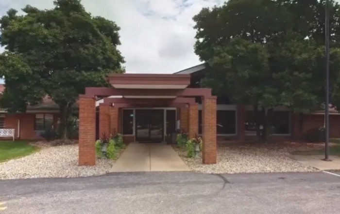 A brick building entrance with a covered pathway surrounded by trees.