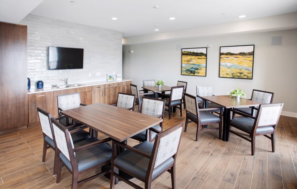 A modern meeting room with multiple tables and chairs, a television mounted on the wall, and artwork displayed.