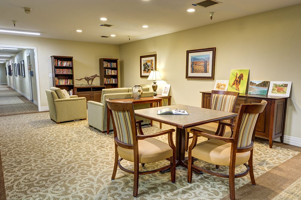 A cozy living room with a table, chairs, sofas, bookshelves, and artwork on the walls.