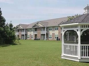 A row of apartment buildings with a grassy lawn and a white gazebo in the foreground.