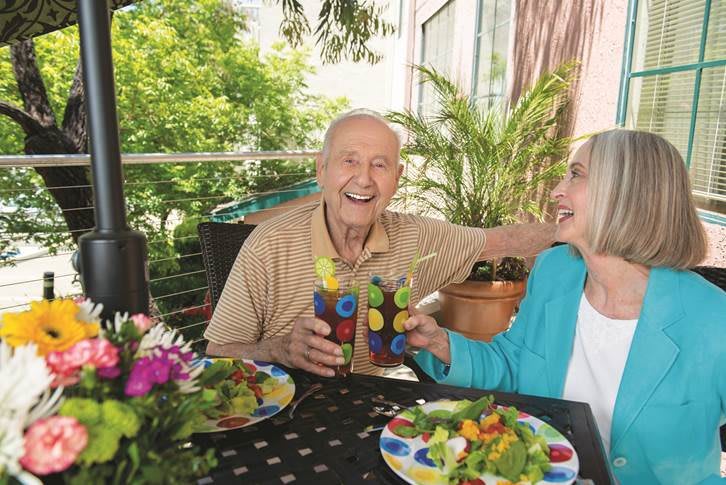 An elderly couple enjoying drinks and salads together in a garden setting.
