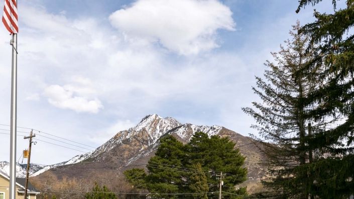 A scenic view of a snow-capped mountain under a cloudy sky, surrounded by lush green trees.