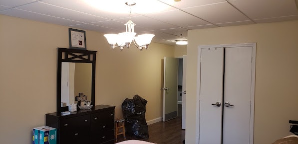 A bedroom interior featuring a chandelier, dresser with mirror, and an open doorway.
