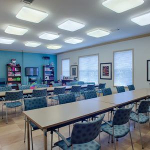 A well-lit classroom or meeting room with tables, chairs, and bookshelves.