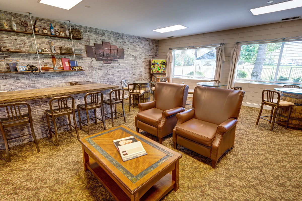 A cozy living room with leather armchairs, a wooden coffee table, and a bookshelf against a brick accent wall.