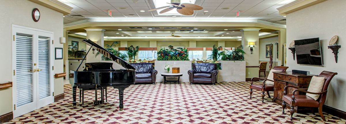 A spacious lobby featuring a grand piano, comfortable leather seating, and lush indoor plants.