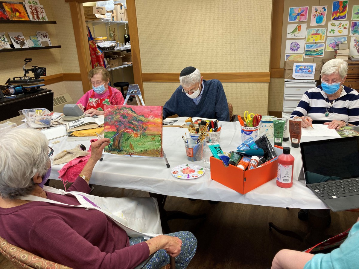 A group of seniors engaged in an art class, painting while wearing masks.