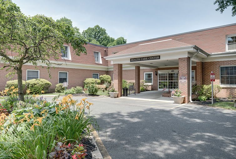 The front entrance of a brick building with landscaped gardens and flowers.