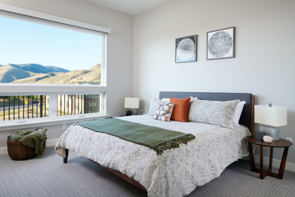 A bright and cozy bedroom with a neatly made bed, decorative pillows, and two framed artworks on the wall, featuring a window view of a scenic landscape.