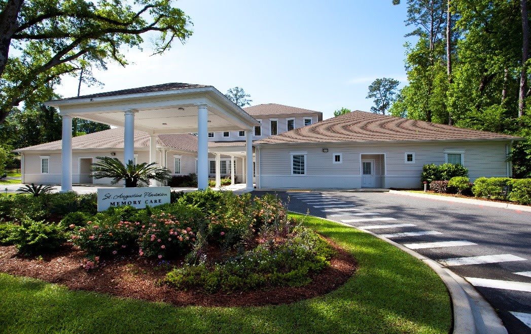 A spacious white building with well-maintained landscaping and a driveway, surrounded by trees.