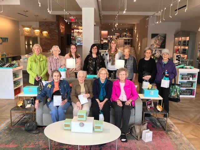 A group of women gathered indoors, seated and standing, in a casual setting.