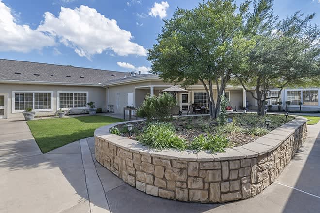 A well-maintained garden area with a stone border and patio in front of a residential building.