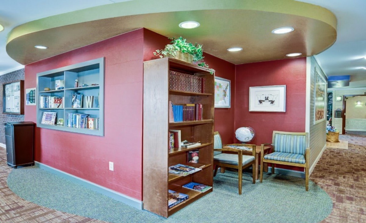 A cozy waiting room with a bookshelf and chairs against red walls.