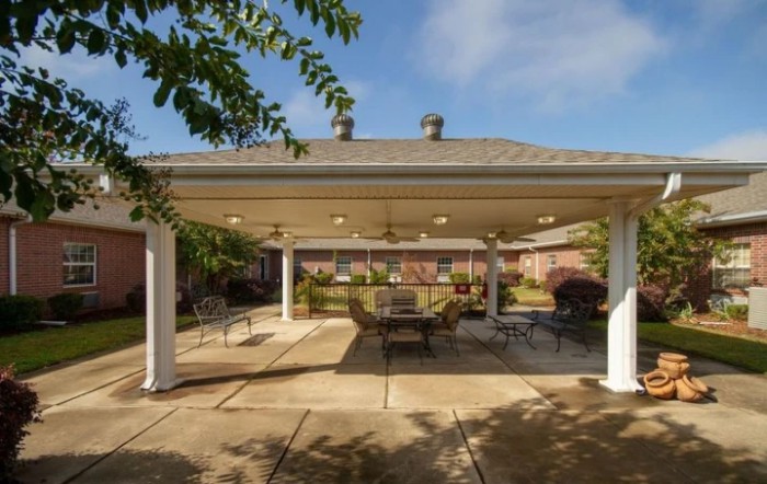 A spacious outdoor patio with a gazebo, featuring comfortable seating and surrounded by greenery on a sunny day.