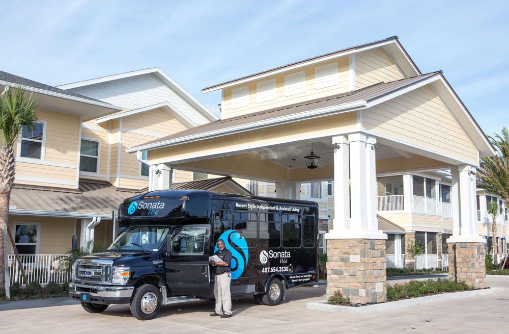 A shuttle bus parked at the entrance of a building, with a person standing nearby.